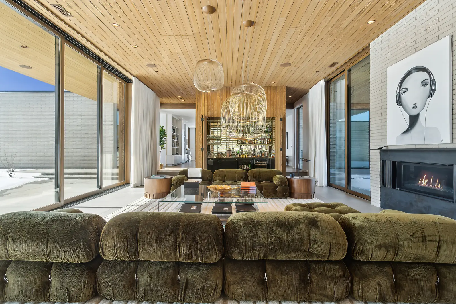 Great room with a green velvet sectional, a fireplace beneath a large portrait, and a built-in bar in a Park City home managed by Life Elevated